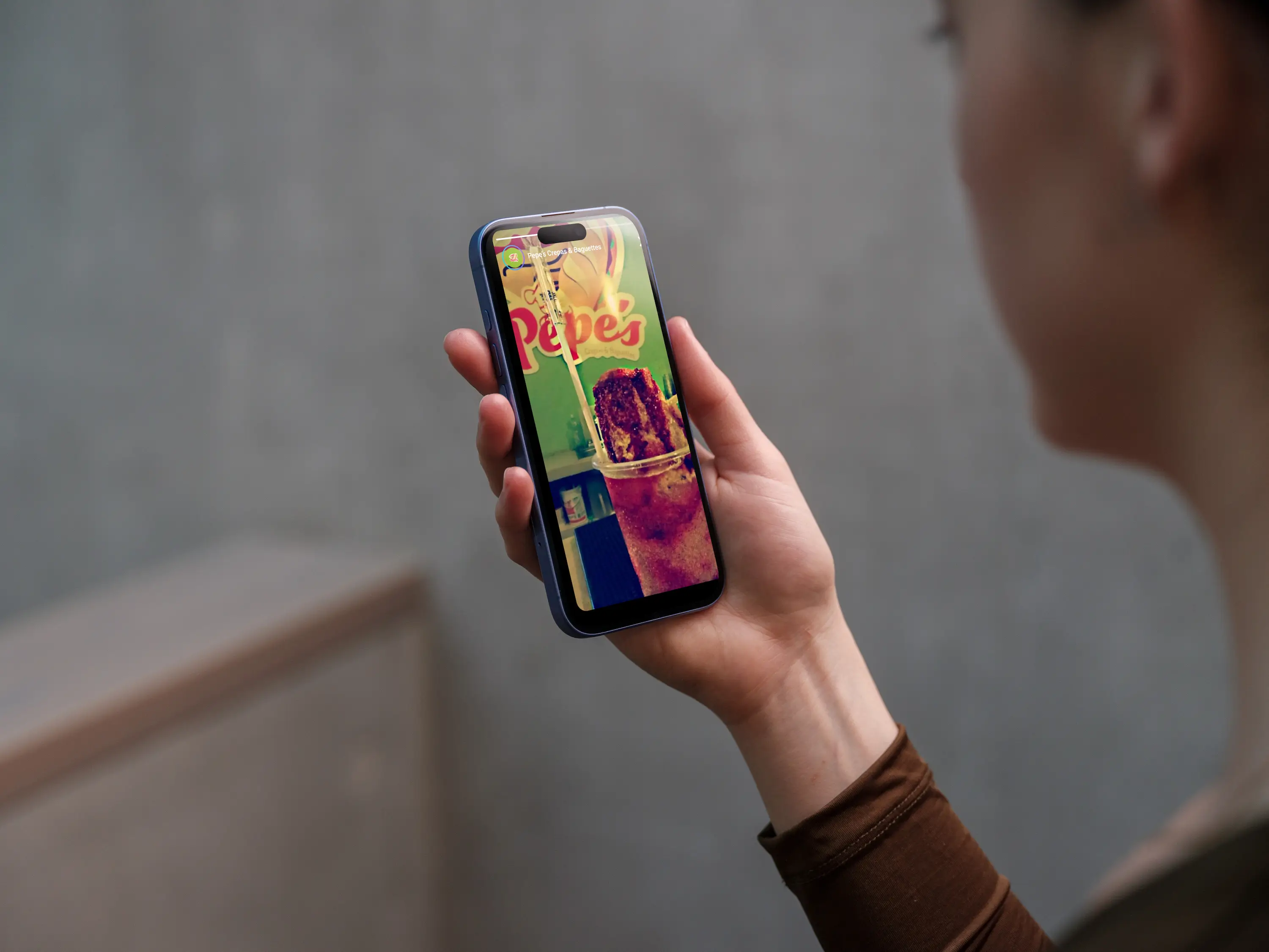 Photograph of a hand holding a phone displaying a Pepe's Instagram story featuring a drink with the logo in the background.
